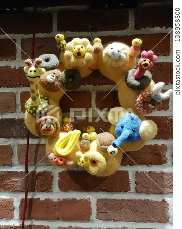 羊毛氈動物花環,一件手工製作的作品,展示在磚牆上。 羊毛氈動物花環,一件手工製作的作品,展示在磚牆上。 138958800