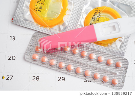 Pregnancy test with birth control pills and condom for female on calendar, ovulation day. Pregnancy test with birth control pills and condom for female on calendar, ovulation day. 138959217
