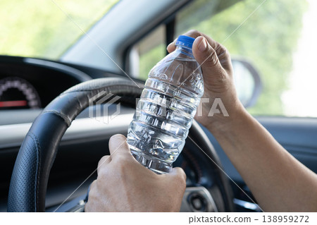 Asian woman driver hold cold water for drink in car, dangerous and risk an accident. 138959272