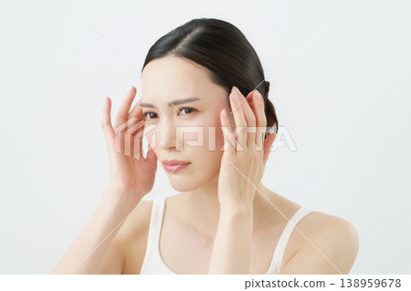 A young Japanese woman touching her head against a white background. 138959678