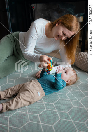 Happy mother playing with her infant baby boy on the floor at home Happy mother playing with her infant baby boy on the floor at home 138960023