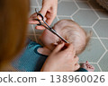 Close-up of a mother carefully trimming her baby son's hair with scissors 138960026