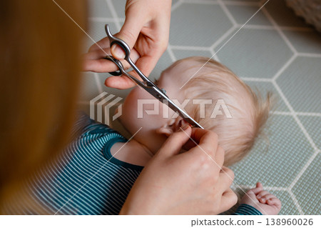 Close-up of a mother carefully trimming her baby son's hair with scissors Close-up of a mother carefully trimming her baby son's hair with scissors 138960026