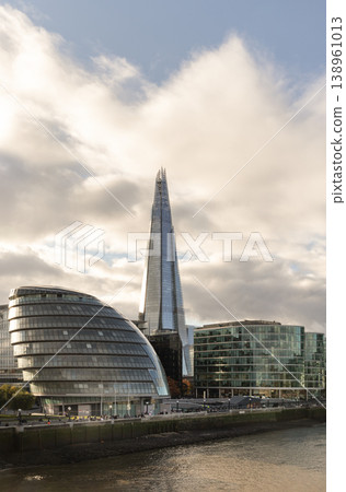 The Shard neo-futurist spire pierces a soft, overcast sky, its glass facade shimmering with the muted light of a London afternoon. Beside it, the bulbous silhouette of City Hall provides a fluid, The Shard neo-futurist spire pierces a soft, overcast sky, its glass facade shimmering with the muted light of a London afternoon. Beside it, the bulbous silhouette of City Hall provides a fluid, 138961013