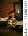 Woman holding phone to head sitting on bed while man reflected in mirror in background 138961182