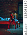 Young woman sitting on bed with glass of wine in dramatic red blue lighting moody interior. 138961189