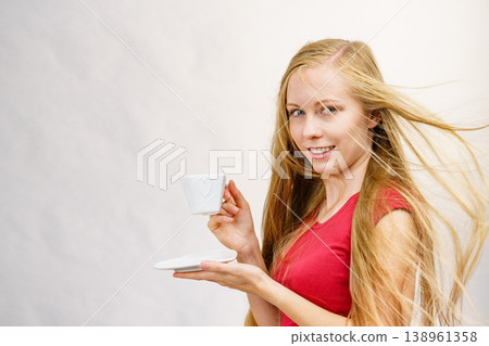 Blonde girl blowing hair holds coffee cup 138961358