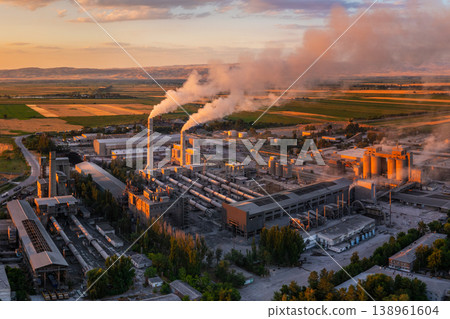 Industrial cement plant with smokestacks and agricultural fields at sunset, drone POV Industrial cement plant with smokestacks and agricultural fields at sunset, drone POV 138961604