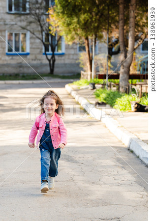 Little girl walking alone on residential street wearing pink jacket and denim overalls during daytime in urban neighborhood. Concept of childhood independence lifestyle movement and outdoor activity Little girl walking alone on residential street wearing pink jacket and denim overalls during daytime in urban neighborhood. Concept of childhood independence lifestyle movement and outdoor activity 138961939