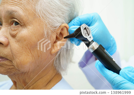 Otolaryngologist or ENT physician doctor examining senior patient ear with otoscope, hearing loss problem. 138961999