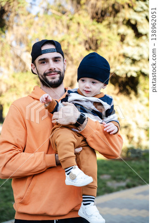 Father holding toddler boy in arms outdoors in park while both look at camera and child points forward. Concept of parenting and family care 138962051