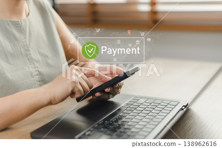 Woman using smartphone and laptop for secure online payment with virtual icon interface. Concept of mobile banking, digital transaction, e-commerce security, and financial technology at home Woman using smartphone and laptop for secure online payment with virtual icon interface. Concept of mobile banking, digital transaction, e-commerce security, and financial technology at home 138962616
