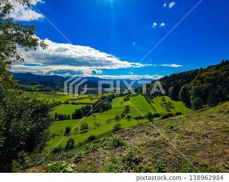 Panoramic view of a small town in a lush green valley at the foot of blue mountains. Panoramic view of a small town in a lush green valley at the foot of blue mountains. 138962984