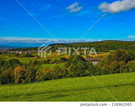 Panoramic view of a small town in a lush green valley at the foot of blue mountains. Panoramic view of a small town in a lush green valley at the foot of blue mountains. 138962985