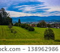 Panoramic view of a small town in a lush green valley at the foot of blue mountains. 138962986