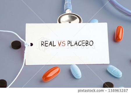 A white tag displays REAL VS PLACEBO surrounded by assorted pills and a blue stethoscope on a grey background. This illustrates clinical trial differences A white tag displays REAL VS PLACEBO surrounded by assorted pills and a blue stethoscope on a grey background. This illustrates clinical trial differences 138963287