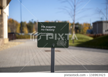 Green warning sign asking not to walk on the grass, placed in a landscaped urban area with blurred background. Green warning sign asking not to walk on the grass, placed in a landscaped urban area with blurred background. 138963423