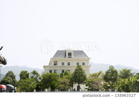 Elegant white house with classic architecture, surrounded by green trees, under clear sky with mountains in the background. Elegant white house with classic architecture, surrounded by green trees, under clear sky with mountains in the background. 138963527