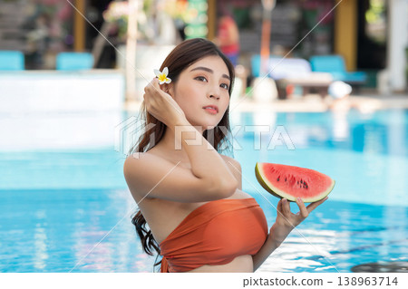 Very Beautiful woman with flower relaxing in swimming pool and eating watermelon. Sexy young asian woman in swimsuits in summer. Very Beautiful woman with flower relaxing in swimming pool and eating watermelon. Sexy young asian woman in swimsuits in summer. 138963714