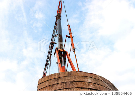 Low angle view of a construction crane lifting structure above concrete tower against sky. Industrial building and engineering scene with strong perspective and copy space 138964406