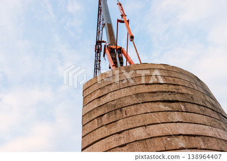Low angle view of a construction crane lifting structure above concrete tower against sky. Industrial building and engineering scene with strong perspective and copy space 138964407