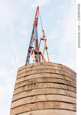 Low angle view of a construction crane lifting structure above concrete tower against sky. Industrial building and engineering scene with strong perspective and copy space Low angle view of a construction crane lifting structure above concrete tower against sky. Industrial building and engineering scene with strong perspective and copy space 138964408