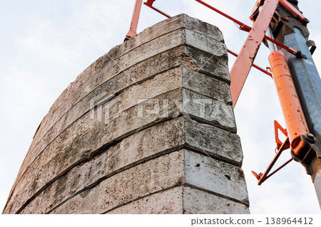 Low angle close up of stacked concrete blocks with an orange crane boom against a cloudy sky. Industrial construction and heavy lifting with strong perspective. Low angle close up of stacked concrete blocks with an orange crane boom against a cloudy sky. Industrial construction and heavy lifting with strong perspective. 138964412