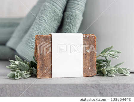 Brown solid soap bar with blank paper label mockup near with leaves and sage green bath towel 138964448