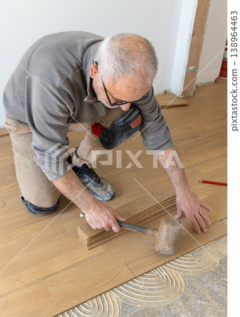 Professional carpenter installing parquet planks during hardwood flooring installation in an apartment 138964463