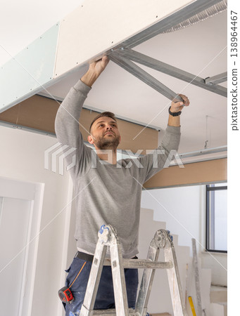 Construction worker installs metal profile frame for drywall suspended ceiling system in apartment Construction worker installs metal profile frame for drywall suspended ceiling system in apartment 138964467