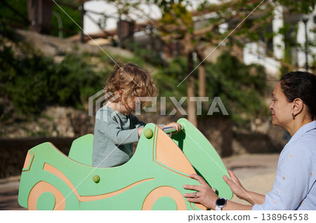 Mother Playing With Toddler On Green Wooden Car At Outdoor Playground 138964558