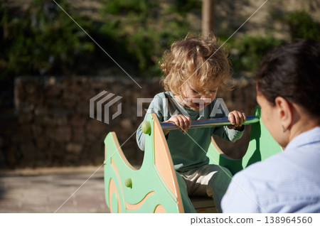 Toddler Playing on Seesaw at Outdoor Playground With Parent Supervising in Sunny Park Toddler Playing on Seesaw at Outdoor Playground With Parent Supervising in Sunny Park 138964560