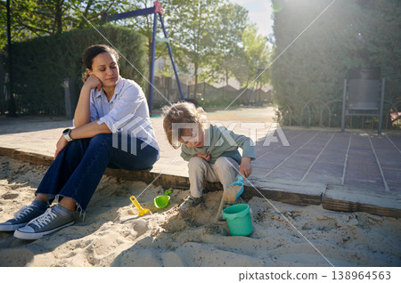 Mother Watching Child Play in Sandbox at Sunny Park 138964563