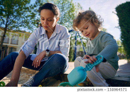 Mother And Toddler Playing Together In A Sunny Sandbox At A Neighborhood Park 138964571