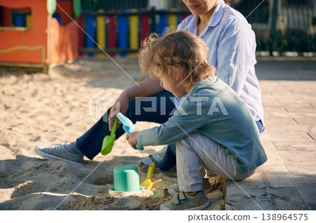 Mother And Child Playing Together In Playground Sandbox On Sunny Day 138964575