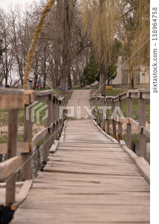 Rustic Wooden Plank Bridge Leading Through a Peaceful Garden with Willow Trees and Calm Water Rustic Wooden Plank Bridge Leading Through a Peaceful Garden with Willow Trees and Calm Water 138964758