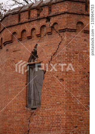 Damaged Red Brick Tower with Large Cracks and Broken Window in Old Architecture Style 138964783