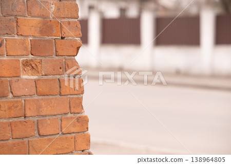 Close up of rustic red brick wall edge with blurred street and white fence background Close up of rustic red brick wall edge with blurred street and white fence background 138964805