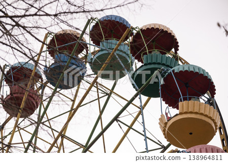 Colorful Carnival Ferris Wheel Gondolas Against Cloudy Sky with Bare Tree Branches Colorful Carnival Ferris Wheel Gondolas Against Cloudy Sky with Bare Tree Branches 138964811