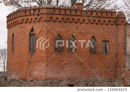 Old Red Brick Tower with Gothic Arched Windows and Large Structural Crack under Overcast Sky 138964829