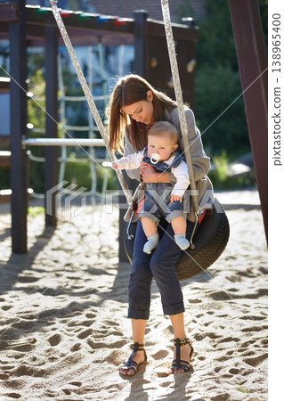 Mother, baby and swing on park for love, bonding and play with sunshine, child development and care. Woman, kid and infant swinging outdoor in summer for fun, enjoyment and nurture with happiness 138965400