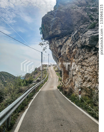 Wide View of Narrow Asphalt Mountain Road Passing Under Overhanging Cliff Wide View of Narrow Asphalt Mountain Road Passing Under Overhanging Cliff 138966155
