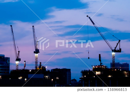 Tower cranes silhouettes and unfinished building construction against night sky Tower cranes silhouettes and unfinished building construction against night sky 138966813