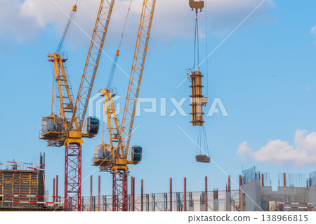 Two yellow tower cranes and unfinished building construction against blue sky 138966815