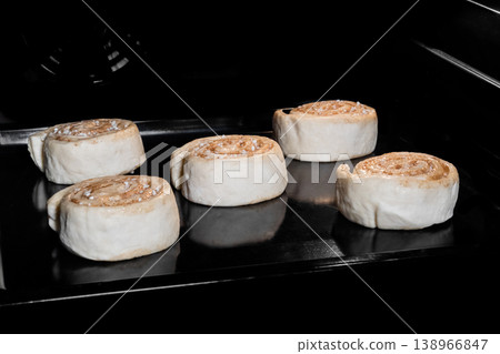 Five uncooked cinnamon buns on tray in electric oven, black background 138966847
