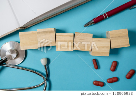 Wooden blocks arranged on a blue background alongside a stethoscope, red capsules, and a pen, symbolizing health, wellness, and the concept of illness management Wooden blocks arranged on a blue background alongside a stethoscope, red capsules, and a pen, symbolizing health, wellness, and the concept of illness management 138966958