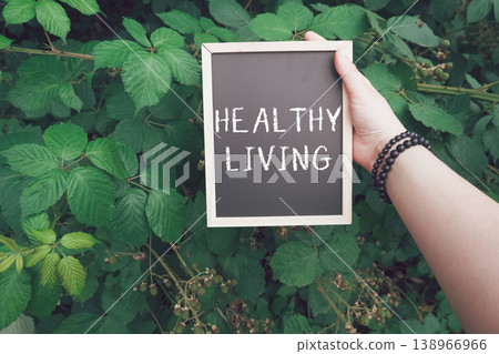 Hand holding a chalkboard sign with the words healthy living surrounded by lush green foliage, symbolizing wellness, vitality, and a connection to nature in a vibrant environment Hand holding a chalkboard sign with the words healthy living surrounded by lush green foliage, symbolizing wellness, vitality, and a connection to nature in a vibrant environment 138966966