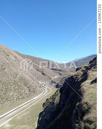 a road among the Landscape of the Caucasus Mountains, North Ossetia, Russia, bright summer day. Rolling green hills and rocky peaks under clear blue sky 138967250