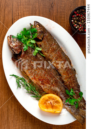 fried fish, rainbow trout, on a white platter with lemon and herbs, no people. fried fish, rainbow trout, on a white platter with lemon and herbs, no people. 138967444