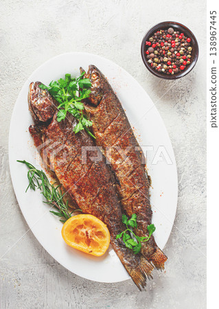 fried fish, rainbow trout, on a white platter with lemon and herbs, no people. fried fish, rainbow trout, on a white platter with lemon and herbs, no people. 138967445